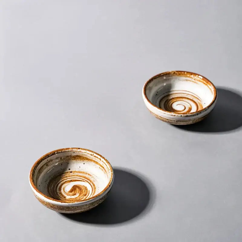 Two small white ceramic seasoning sauce dishes with brown speckled rims and intricate spiral decorbites ceramic seasoning