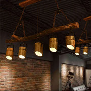 Rustic wood linear island pendant light featuring five brass-colored cylindrical lights hanging from a wooden beam