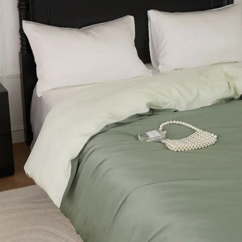 A delicate pearl-embellished handbag with transparent glass body and heart handle rests on a sage green double layer satin queen duvet set