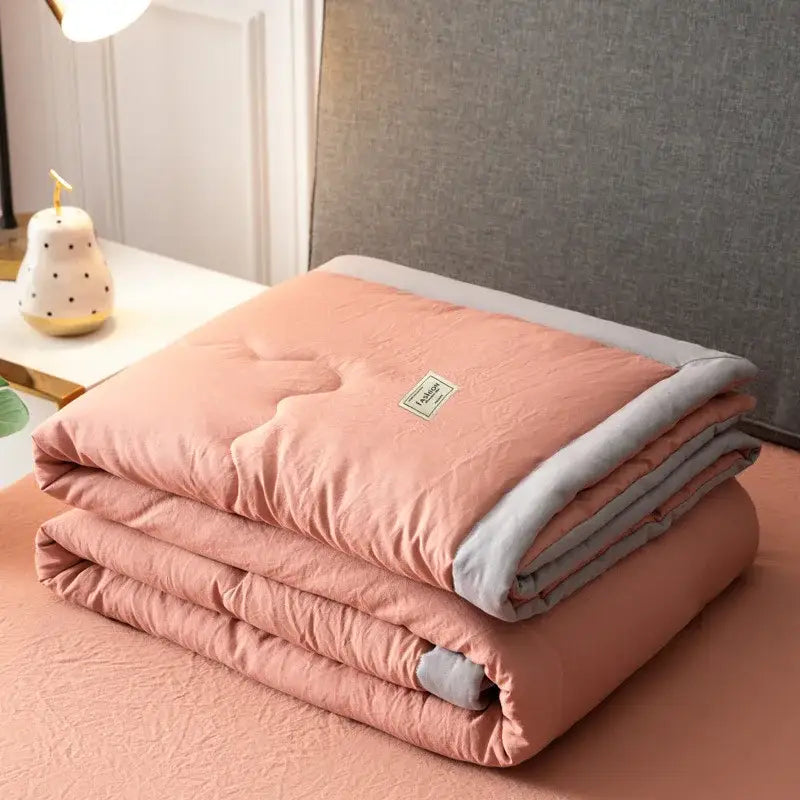 A soft peach-colored decorbites cooling cotton quilt with gray border and subtle stitching for bedroom use