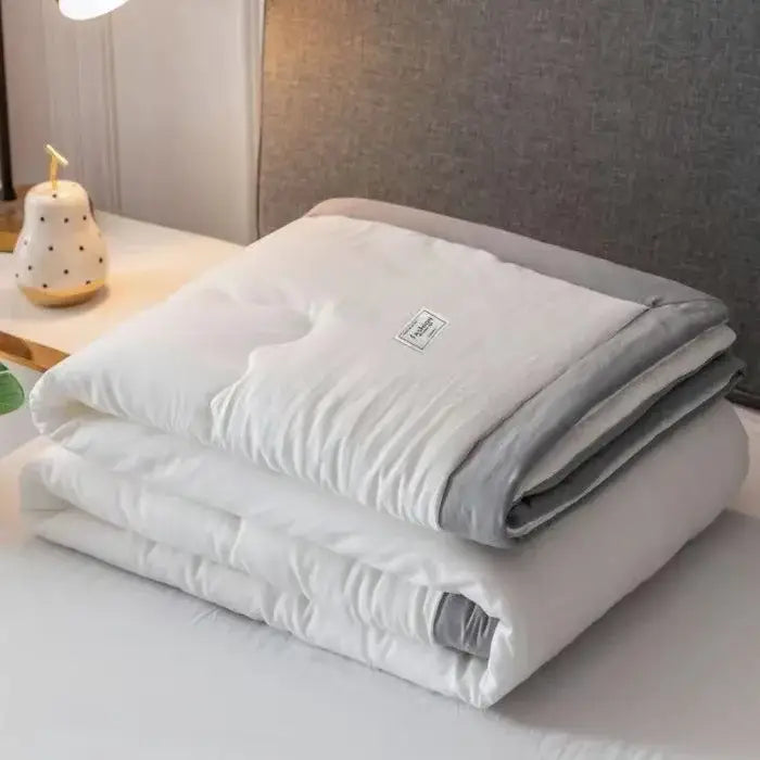 A soft white and gray decorbites cooling cotton quilt with subtle texture and label, ideal as a bedroom blanket