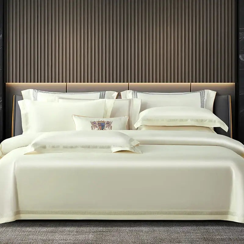 Cream-colored satin egyptian cotton duvet cover set with gold trim and embroidered crest on central pillow