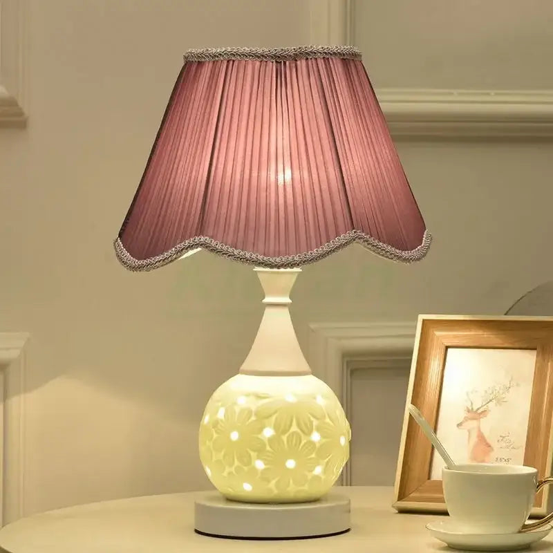A soft pink pleated lampshade with scalloped edge and silver trim on a white floral decorbites ceramic led desk lamp base