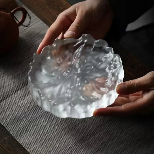 A translucent scalloped crystal glass coaster with floral pattern used as a minimalist jewelry display panel