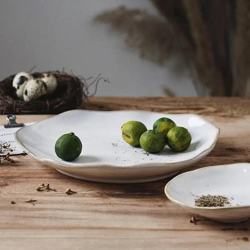 Scalloped white ceramic dinner plate set by decorbites holding green limes for elegant dining tableware use