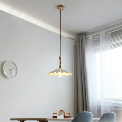 A cream-colored scalloped ceramic led pendant light with brass accents hanging from a wooden fixture for dining room decorbites ceramic led