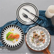 Three black and white geometric ceramic dessert plates including checkered, triangular, and zigzag designs on wood board