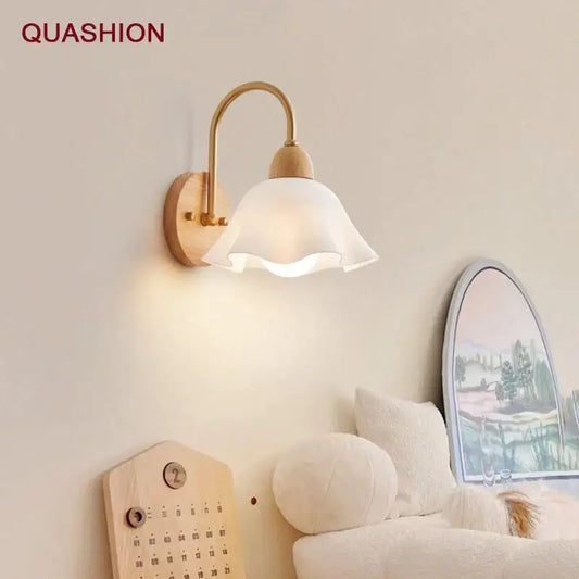 A minimalist scandinavian wall lamp with a white frosted glass shade, brass arm, and cream led wooden base