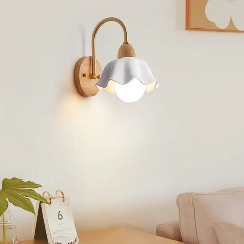 Scandinavian wall lamp with a delicate white ceramic scalloped shade, brass arm, and cream led wooden base decorbites cream led