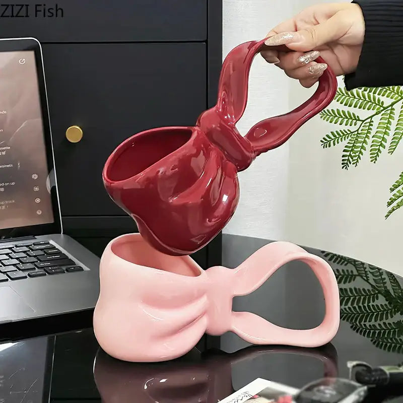 A glossy red decorbites bowknot ceramic coffee mug shaped like a bow with a soft pink counterpart below