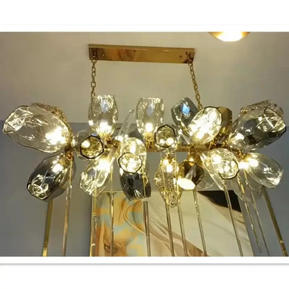 Sculptural gold pendant light with glass shades featuring faceted crystal flower elements and dangling glass rods
