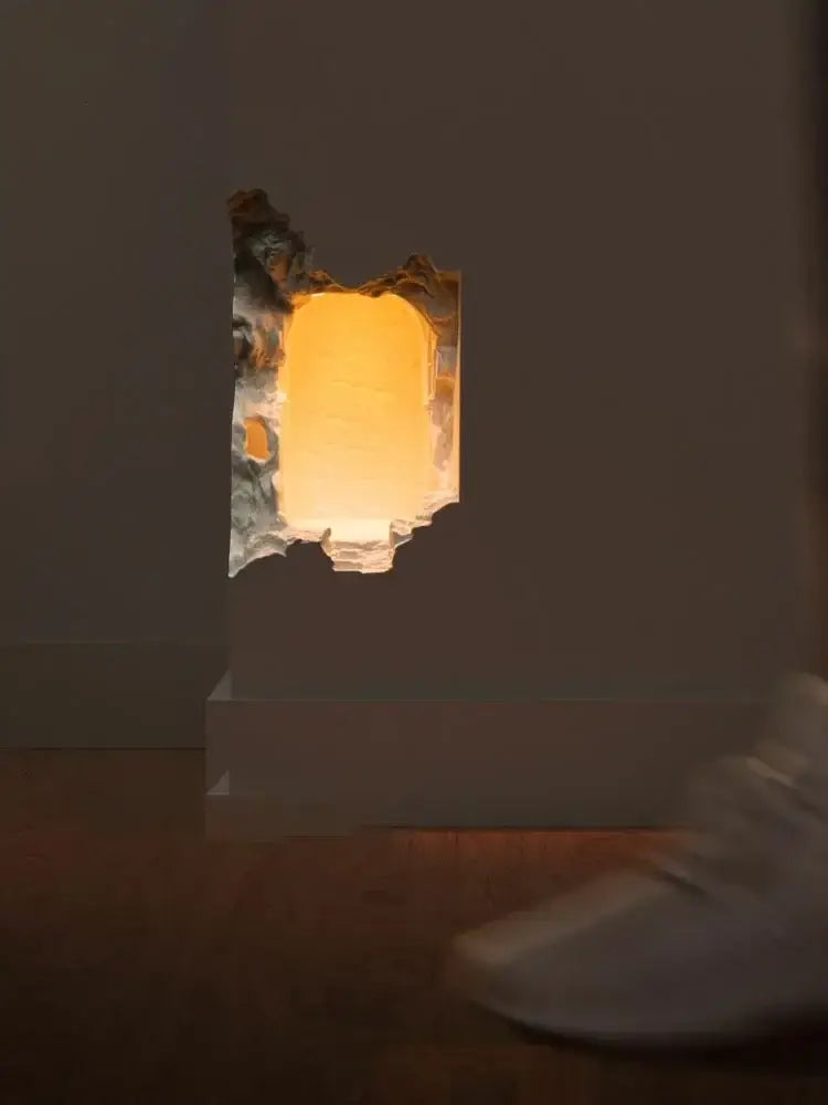 A warm glowing stone embedded night light wall sconce with a rough torn edge frame set into a wall for corridor use
