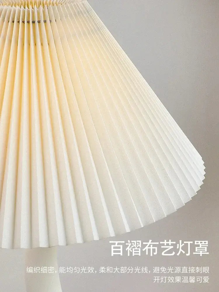 Cream resin floor lamp with a cream-colored pleated fabric lampshade providing soft diffused light from decorbites