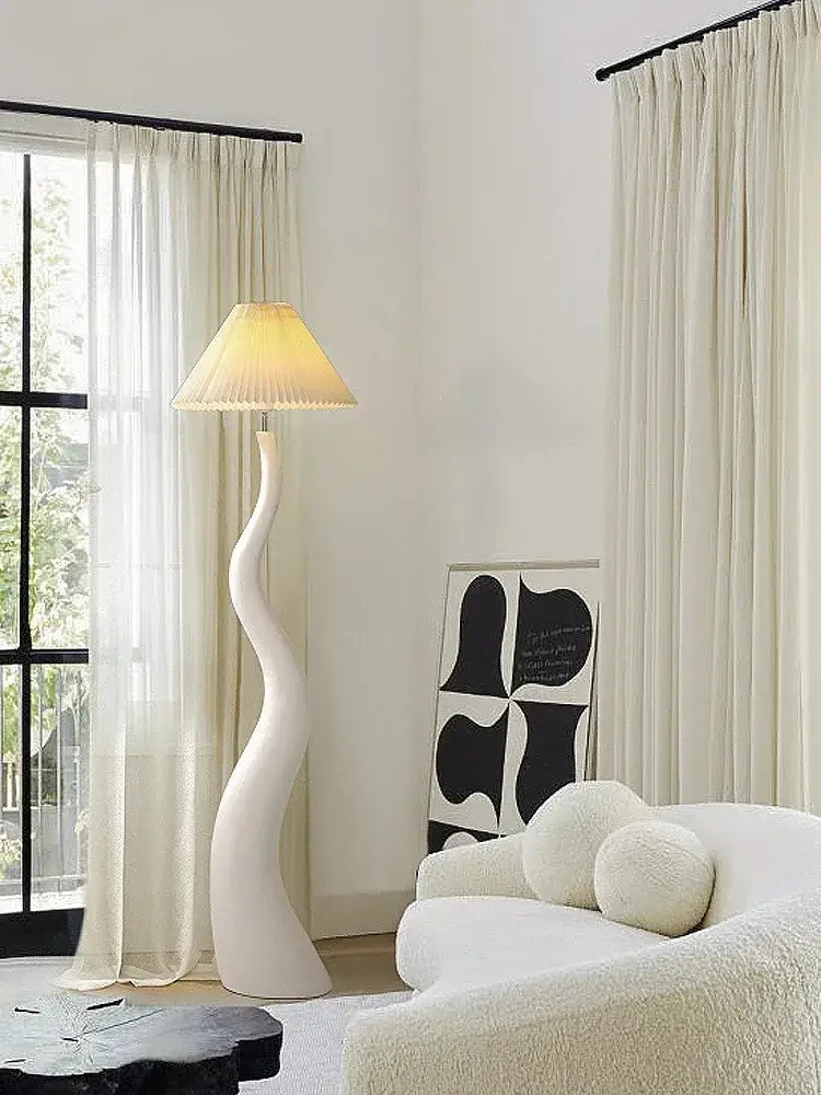 A sleek white floor lamp with a curved sculptural cream resin base and pleated beige shade for living room decorbites cream resin lighting