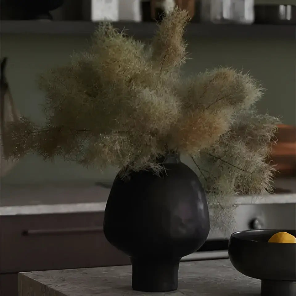 Black matte ceramic vase with dried feathery grasses featuring a sculptural white hammer pattern for living room desk