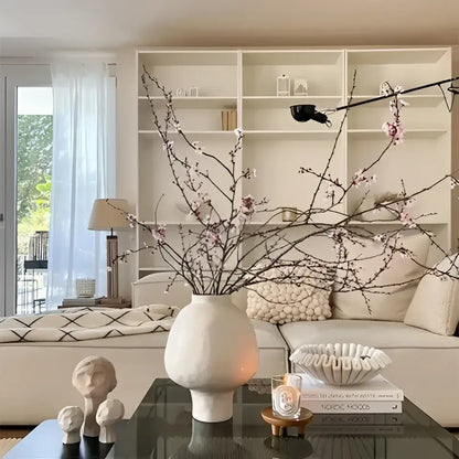 Cream-colored ceramic vase with slender curves and hammer pattern holding delicate pink blossoms for living room desk