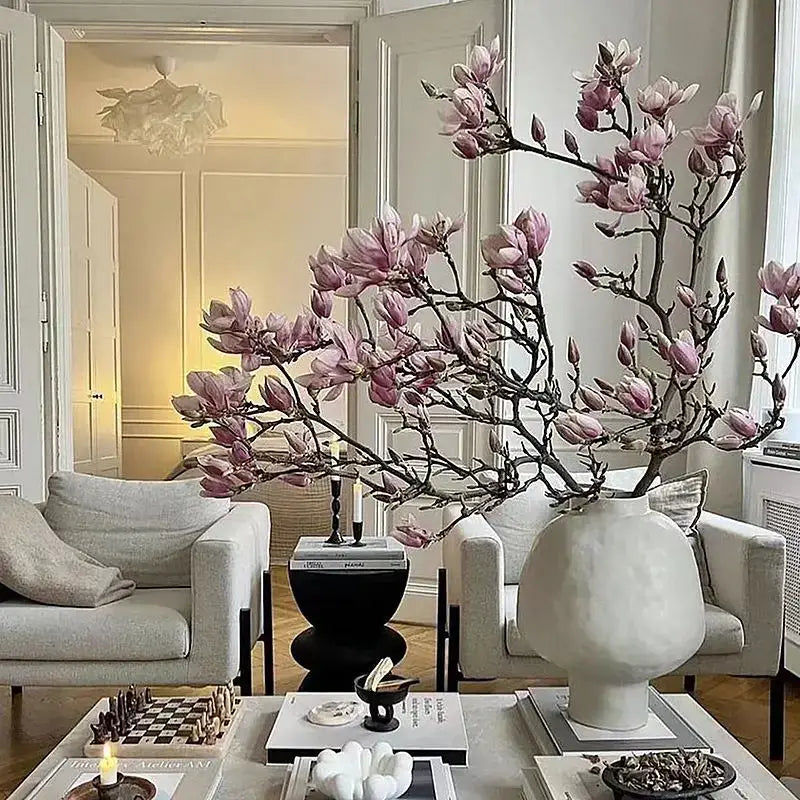 Sculptural white hammer pattern ceramic vase holding pink magnolia blossoms for living room desk decor
