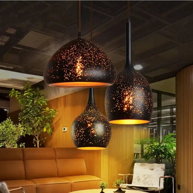 Set of 4 black and gold etched iron pendant light fixtures with speckled starry design and warm amber interiors for dining room