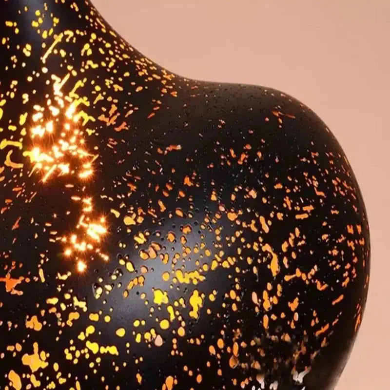 Black ceramic vase with speckled gold and orange glaze finish complementing black and gold etched iron pendant light fixture