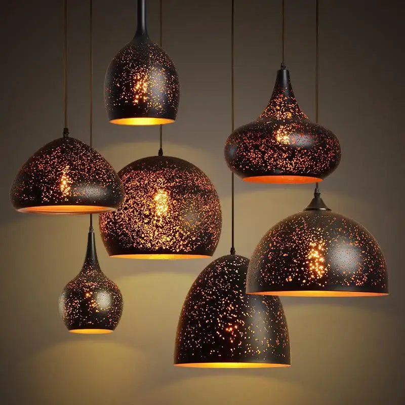 Set of 4 black and gold etched iron pendant light fixtures with speckled starry design and warm amber glow for dining room