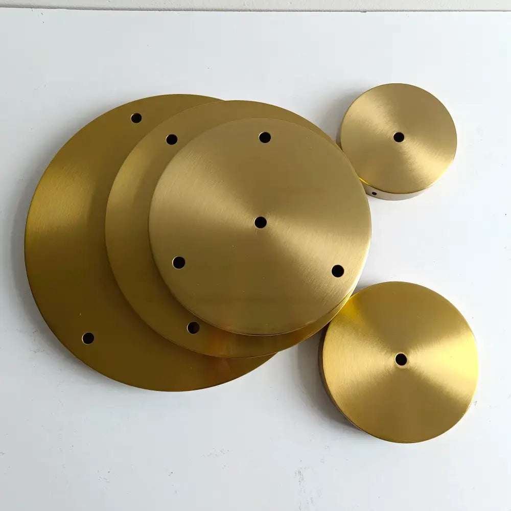 Set of five brushed gold-colored circular metal plates with central and perimeter holes for brass ceiling plate lamp bases