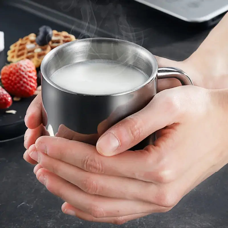 A sleek stainless steel double wall travel mug with curved handle filled with steaming milk for kitchen use