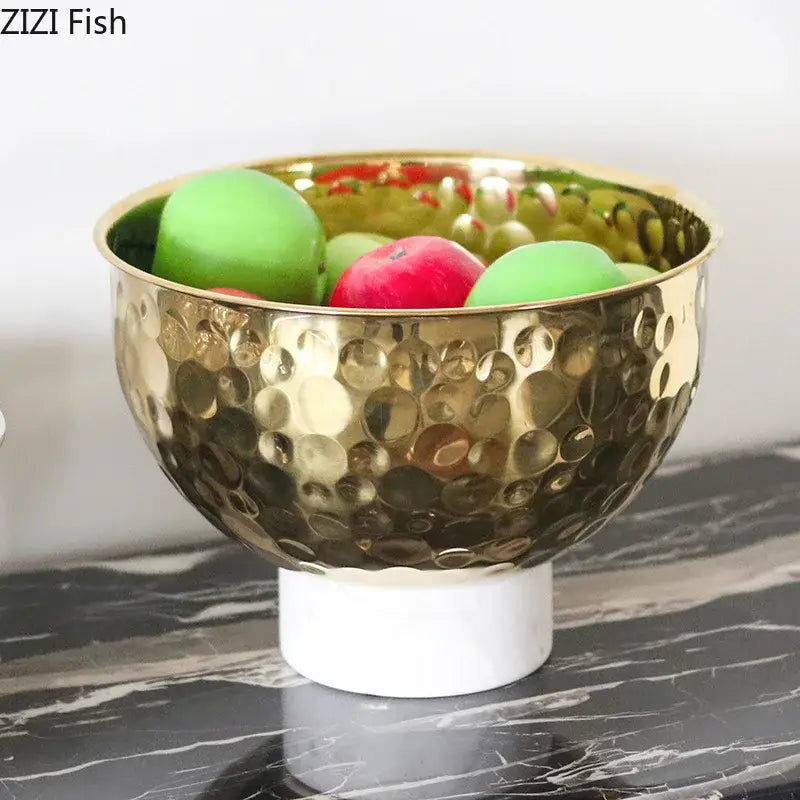 Gold-toned hammered metal fruits bowl with white marble pedestal base featuring hammer pattern for dining room use