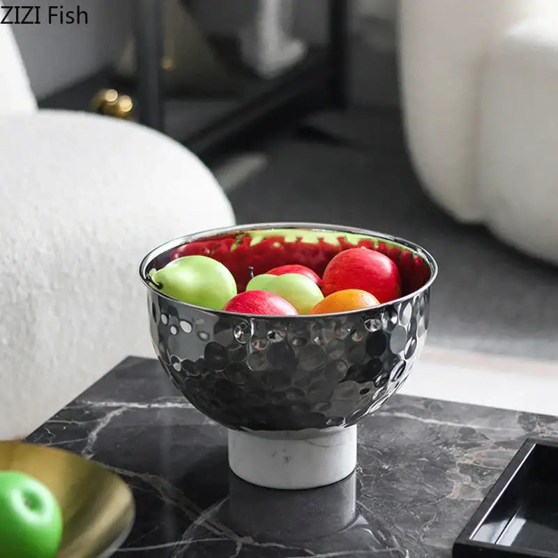 A sleek black hammered metal fruits bowl with a white marble pedestal and reflective red interior for dining room use