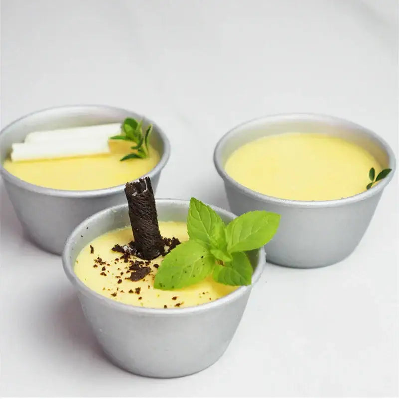 Three silver carbon steel cake molds filled with yellow custard garnished with mint and chocolate decorbites carbon steel