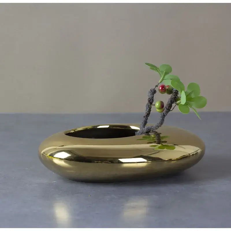 Shiny gold ceramic bonsai pot with minimalist oval design holding small artificial plant in decorbites silver cobblestone ceramic vase