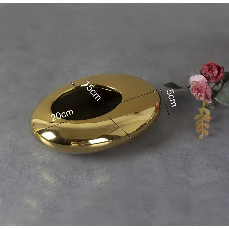 Shiny gold oval ashtray with smooth reflective surface and elongated opening in decorbites silver cobblestone ceramic vase setting