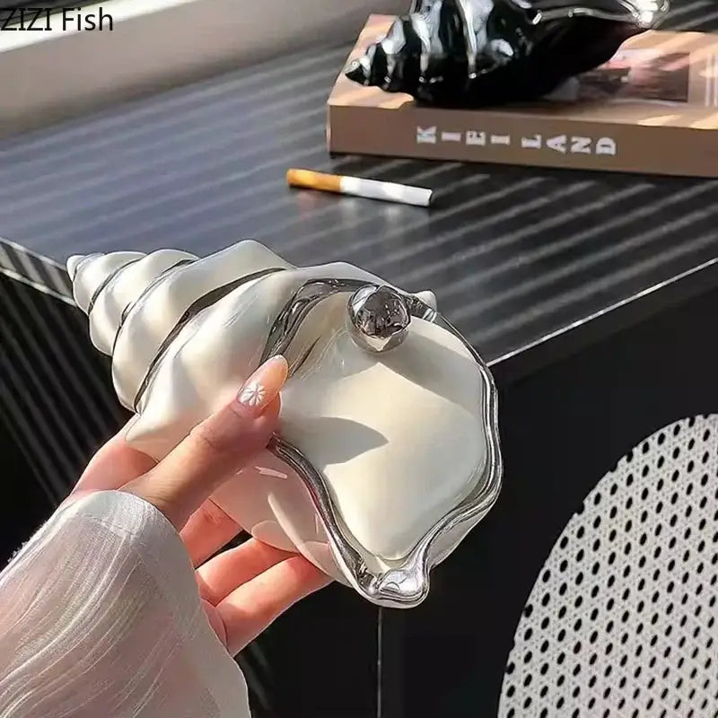 A sleek white ceramic decorbites conch ashtray shaped like a seashell with metallic silver trim and clasp for living room decor
