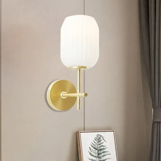 Gold-toned wall sconce light fixture with a cream glass shade and ribbed texture for bedroom use