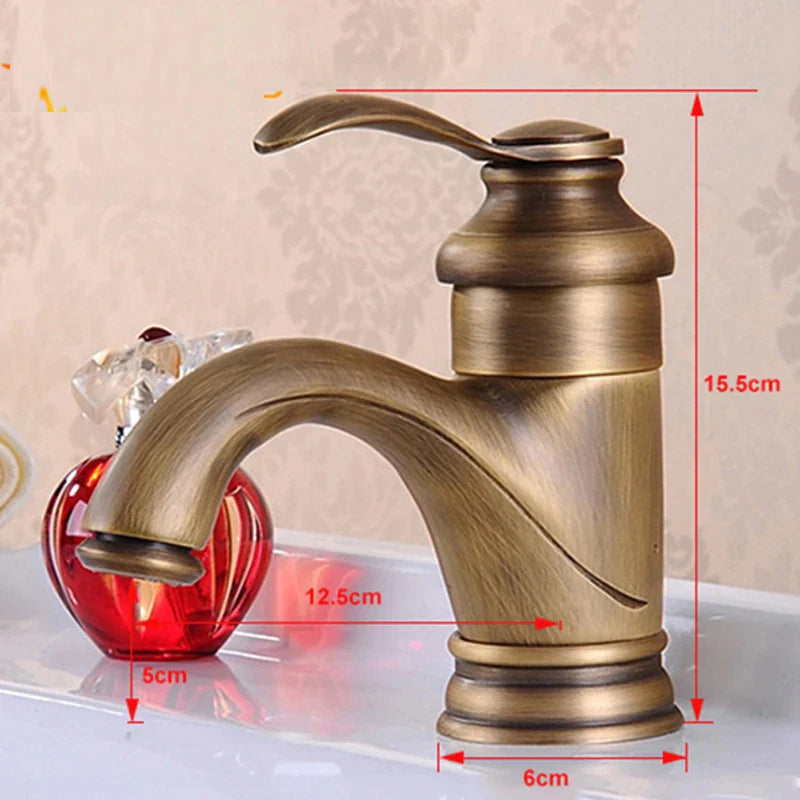 Antique brass single hole deck mounted bathroom faucet with curved spout and decorative crystal apple beside it