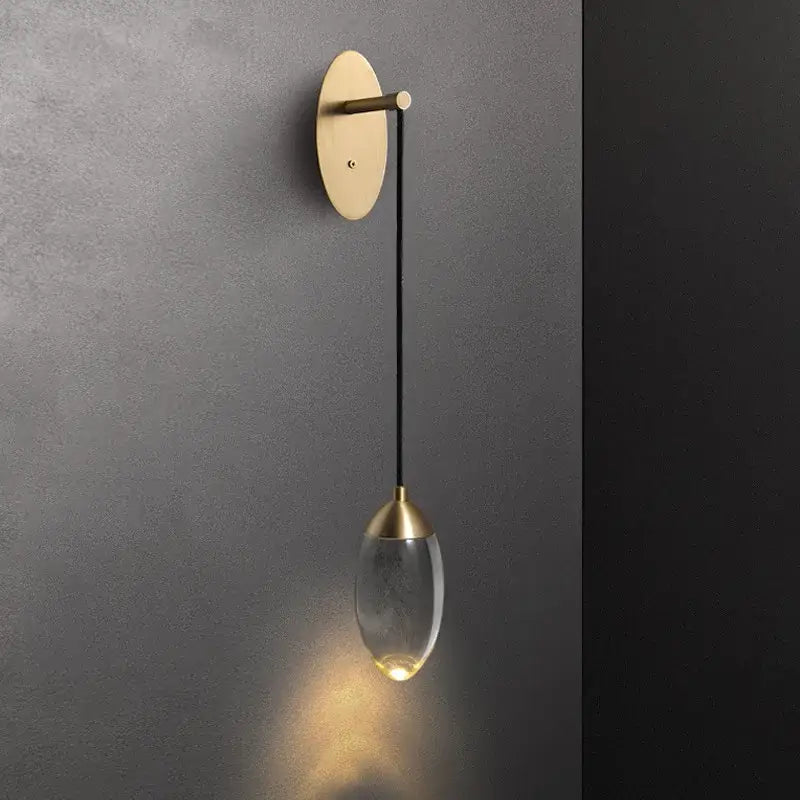 A sleek brass and crystal led wall light with a brushed brass base and teardrop glass pendant for bedroom decorbites crystal led