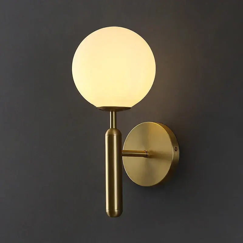 A sleek brass wall sconce lamp with a glowing spherical glass shade designed for corridor lighting