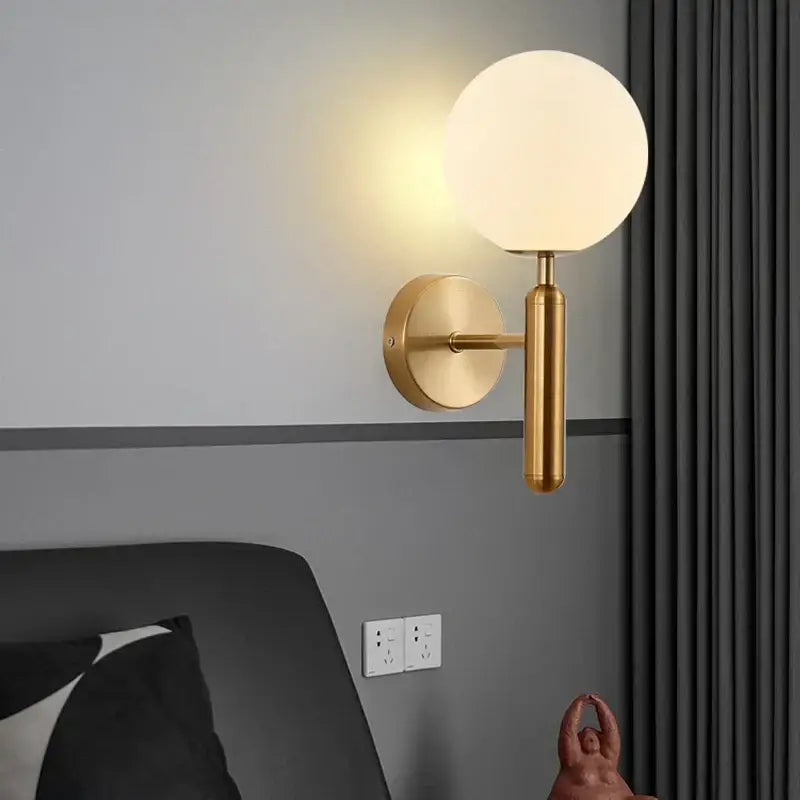 Sleek brass wall sconce lamp with a gold-toned spherical frosted glass globe and cylindrical stem for corridor lighting
