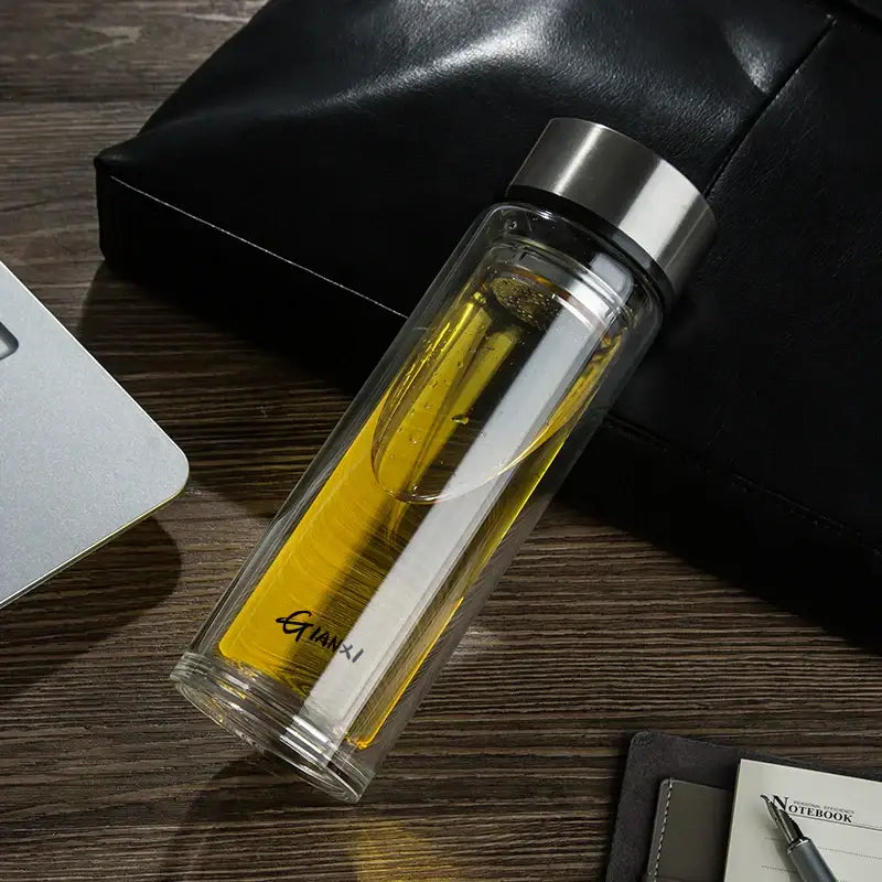 Sleek double-walled glass water bottle with filter filled with golden-yellow liquid and guanxi brand logo etched on side