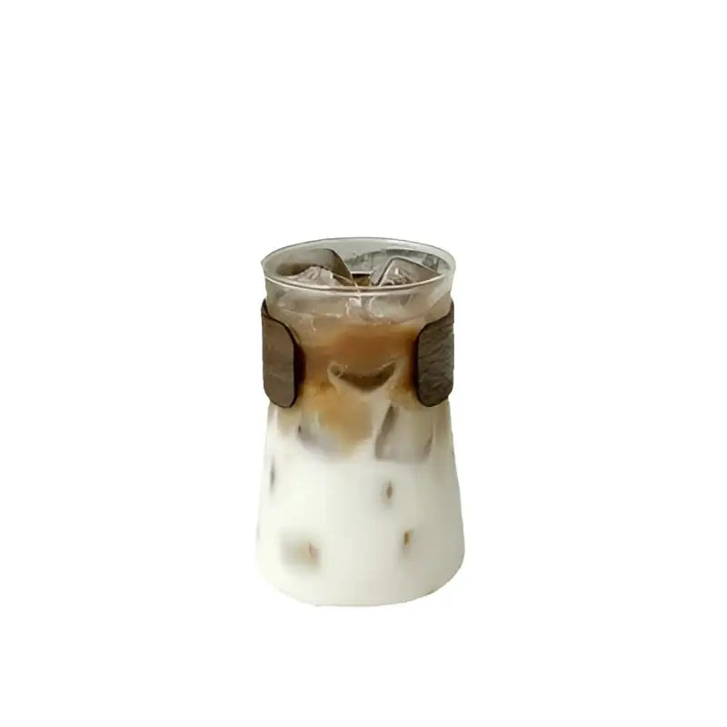 A sleek clear glass iced latte cup with brown leather-like band filled with layered iced latte coffee decorbites glass iced