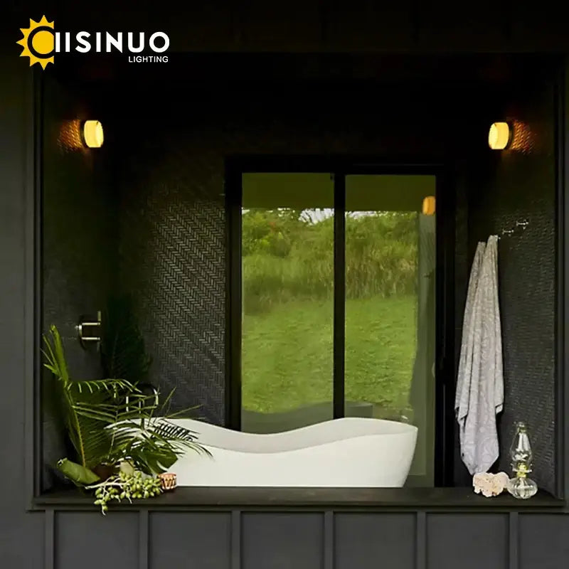 White freestanding bathtub with smooth curved design and glossy finish beside sleek gold round wall sconce glass light soap dish