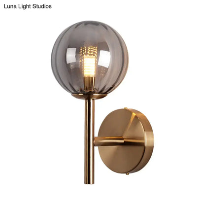 A sleek round wall lighting bedside sconce light with smoked glass globe and brass arm in red green amber tones