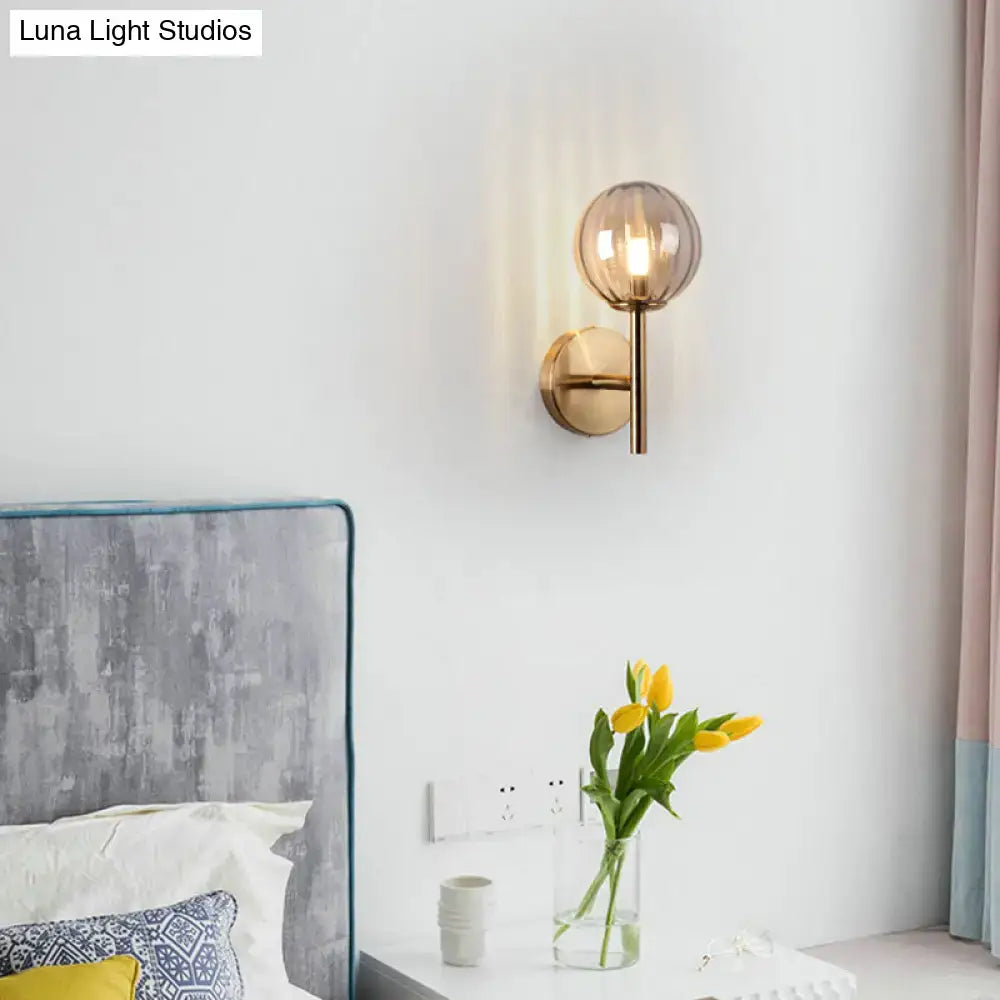 A modern round wall lighting with a spherical amber glass shade and brass base for bedside sconce light use