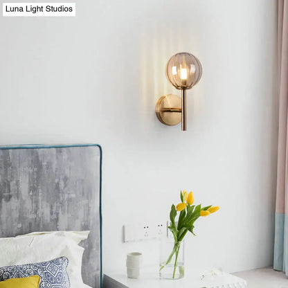A modern round wall lighting with a spherical amber glass shade and brass base for bedside sconce light use