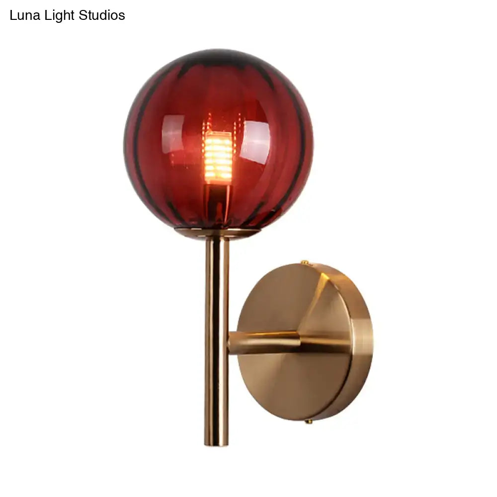 A sleek brass round wall lighting with amber-tinted glass globe and filament bedside sconce light in red green amber