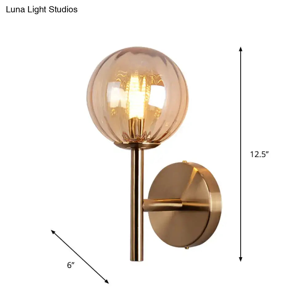 A modern brass round wall lighting with a spherical amber glass globe and exposed filament bulb bedside sconce light