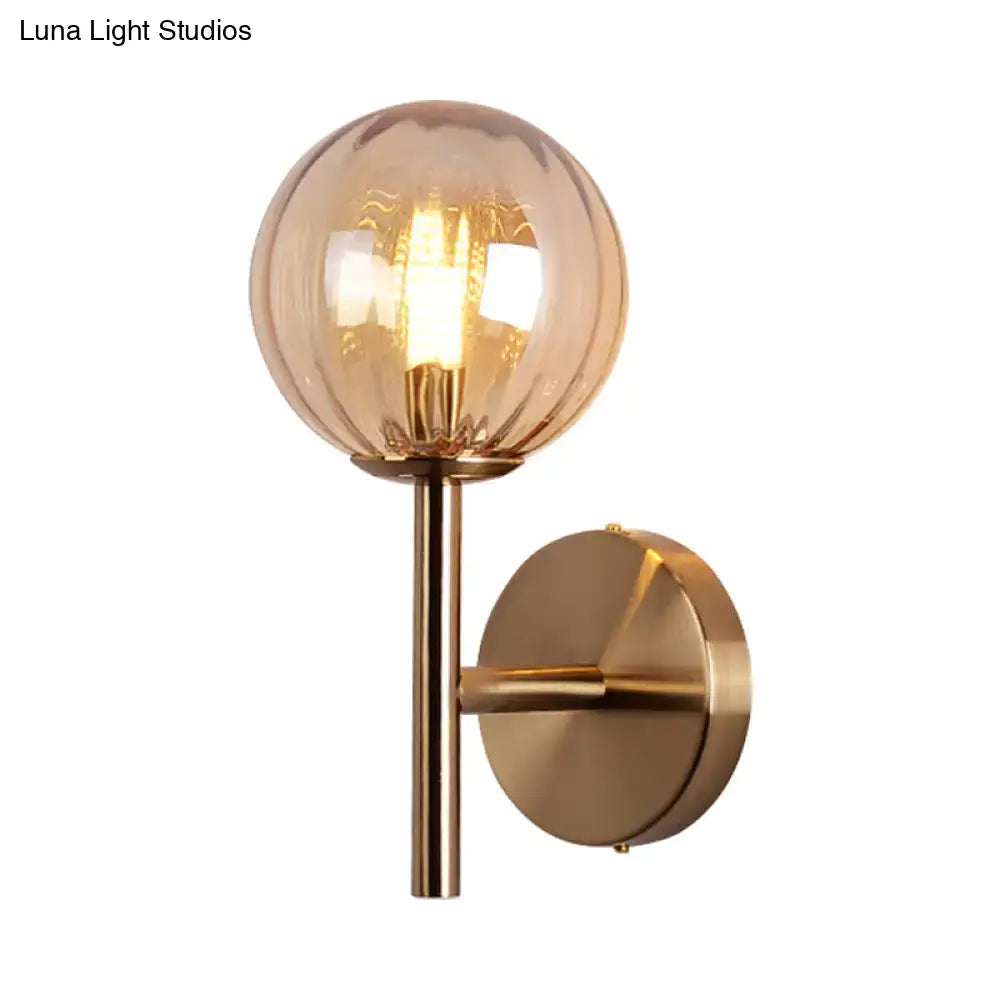 A warm-toned spherical glass globe with vertical ridges on brass stem for sleek round wall lighting red green amber bedside sconce light