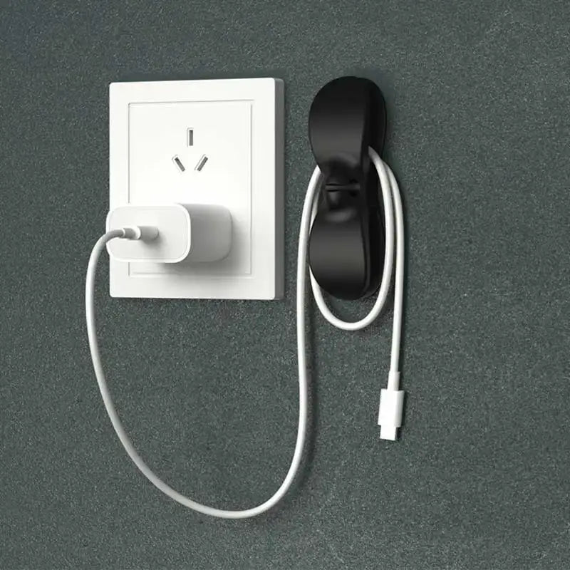 Black silicone decorbites cord winder cable organizer mounted on wall holding a white charging cord in kitchen setting