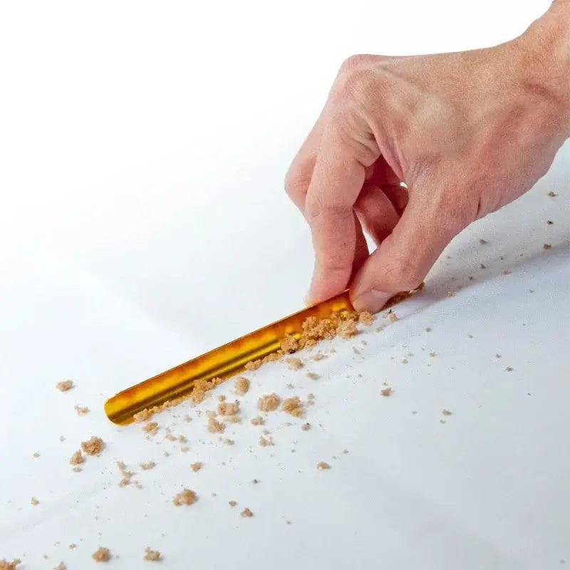 Golden stainless steel crumb cleaner cake tool with smooth reflective surface scraping crumbs from white surface