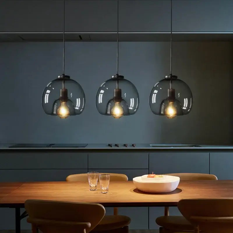 Three hanging pendant lights with dark smoked glass globes and exposed filament bulbs suitable for dining table use