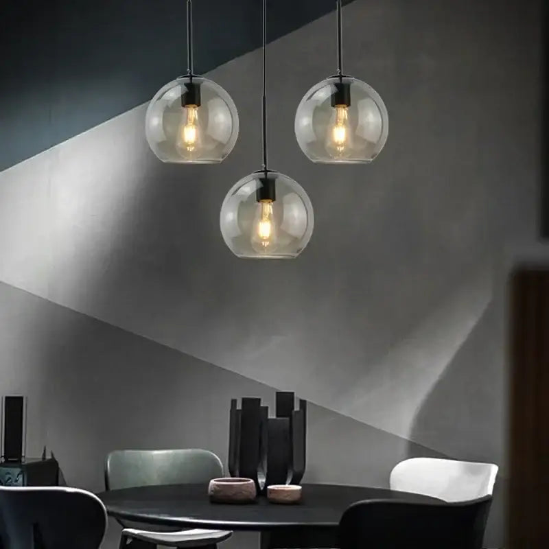 Three smoky gray glass pendant lights with exposed filament bulbs and iron finish cords for dining room lighting